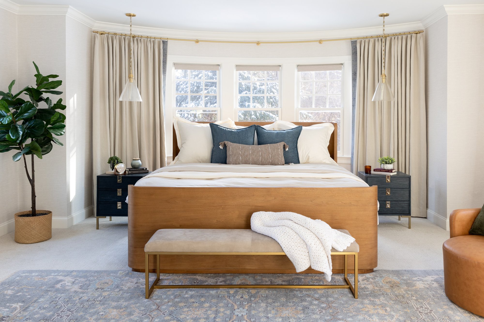 Primary bedroom interior design in Boston featuring a curved bay window, custom wood bed, navy nightstands, and layered neutral bedding Primary bedroom interior design in Boston featuring a curved bay window, custom wood bed, navy nightstands, and layered neutral bedding
