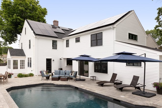 Backyard remodel in Boston with an in-ground pool, patio seating, and a white home exterior with solar panels, designed by Lee Kimball.