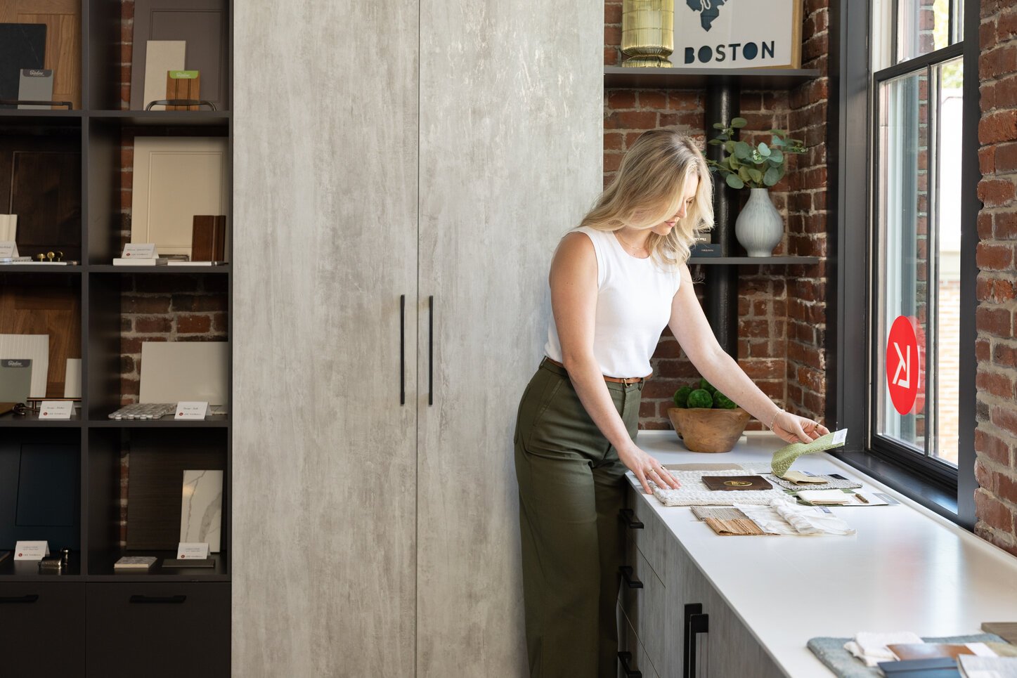 Interior designer reviewing material samples and finishes at the Lee Kimball design showroom in Boston, with exposed brick and material displays in the background.