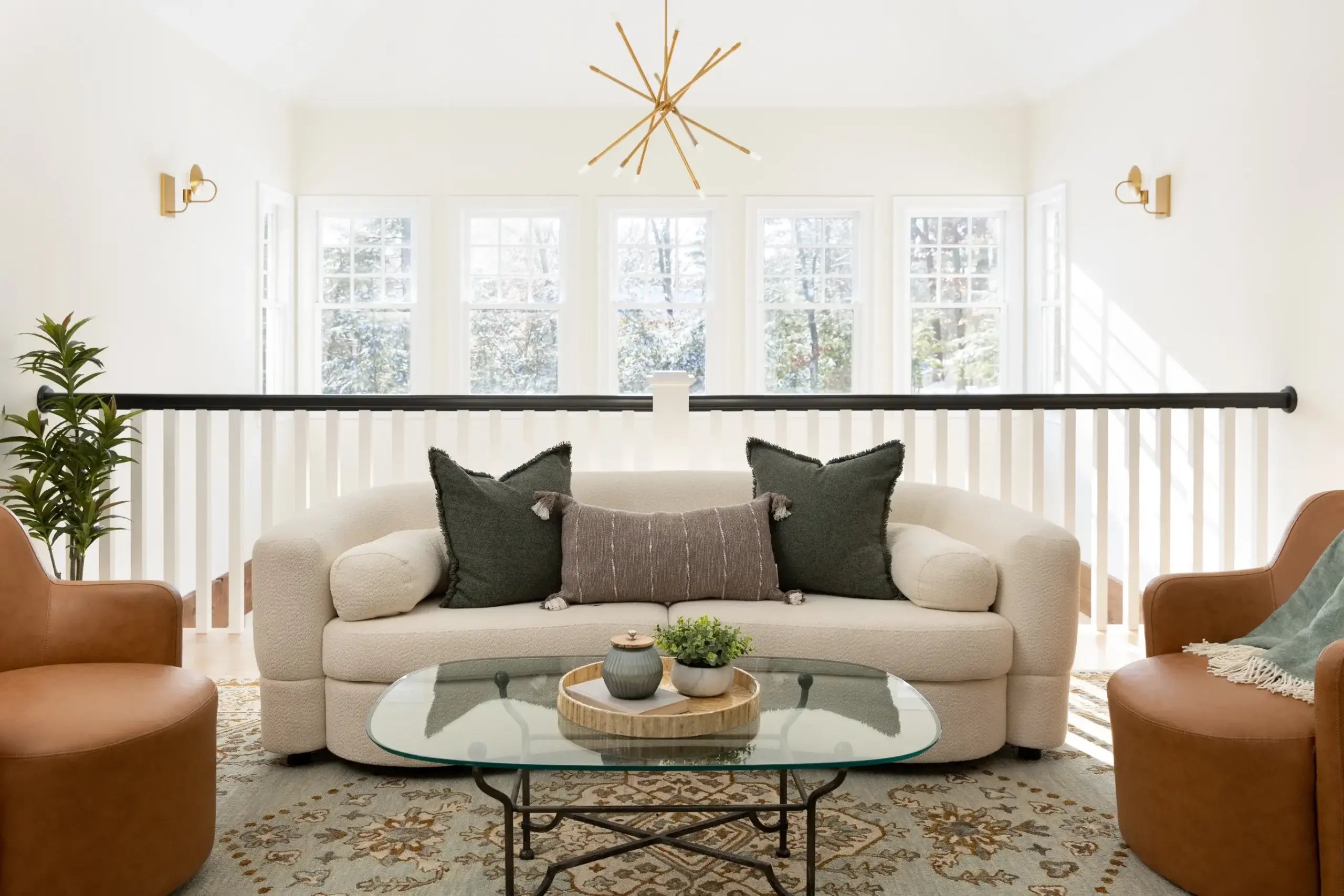 Bright living room in Greater Boston with cream sofa, glass coffee table, and large sunlit windows