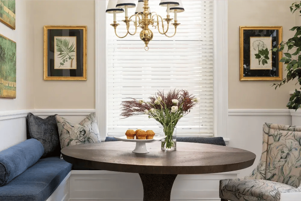 Charming breakfast nook in Greater Boston with round table, blue banquette seating, and brass chandelier Charming breakfast nook in Greater Boston with round table, blue banquette seating, and brass chandelier