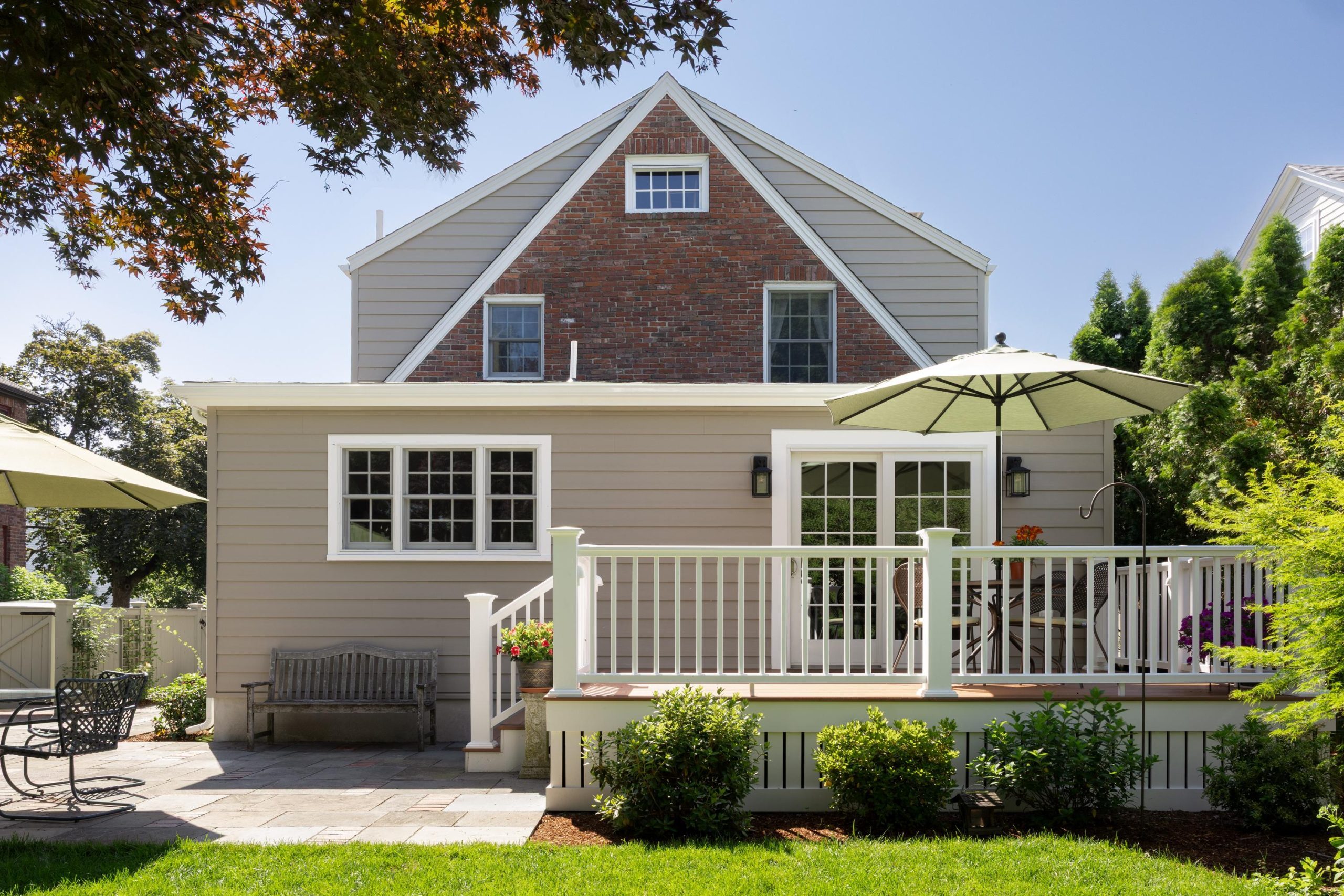 Classic home exterior in Greater Boston with brick gable, backyard deck, patio, and landscaped yard