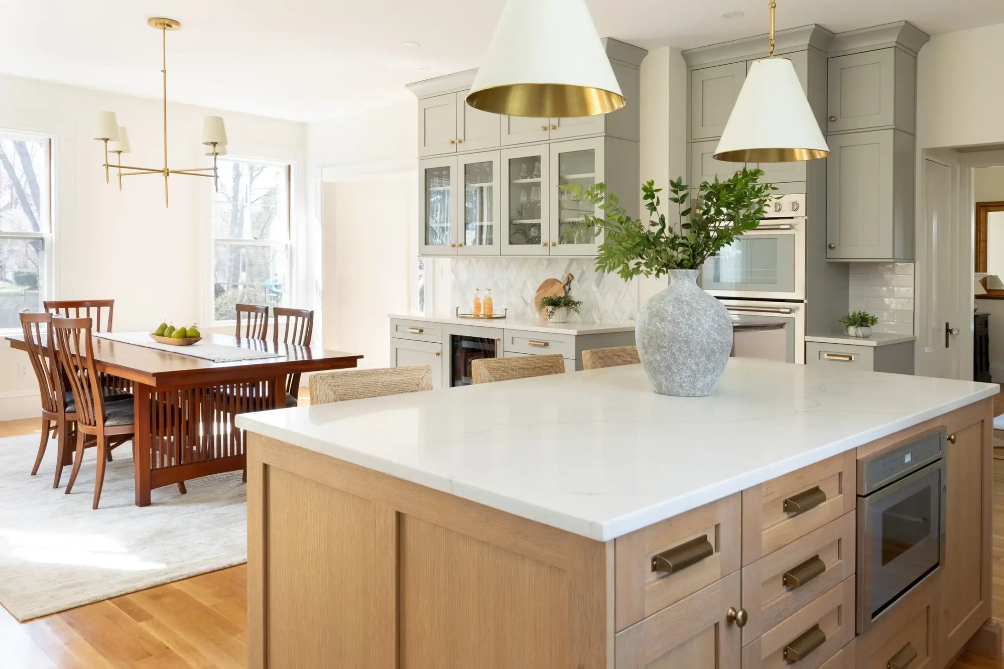 Bright kitchen and dining area in Greater Boston with large island, pendant lights, and classic cabinetry Bright kitchen and dining area in Greater Boston with large island, pendant lights, and classic cabinetry
