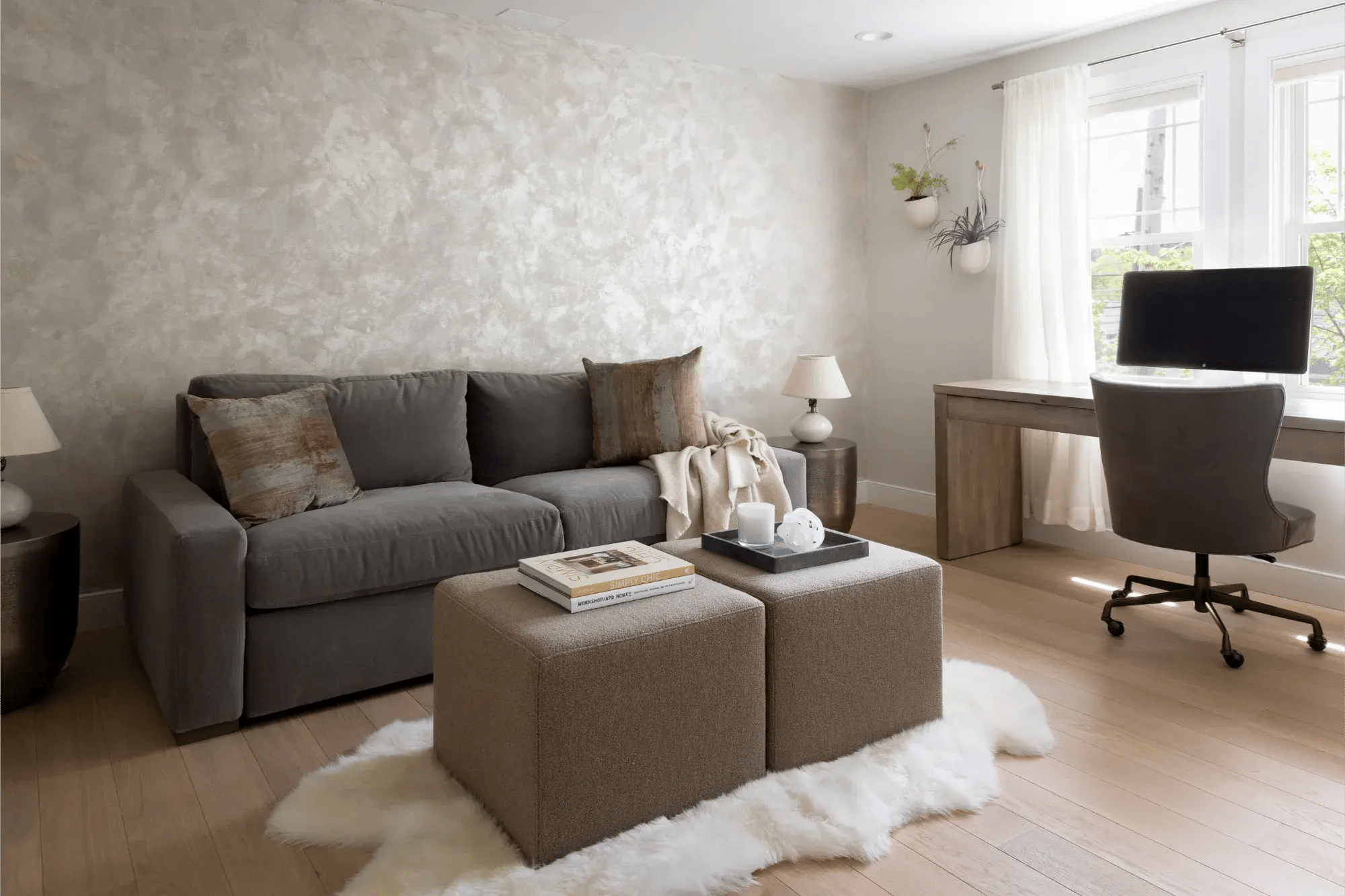 Cozy home office in Greater Boston with gray sofa, ottomans, wood desk, and bright window light
